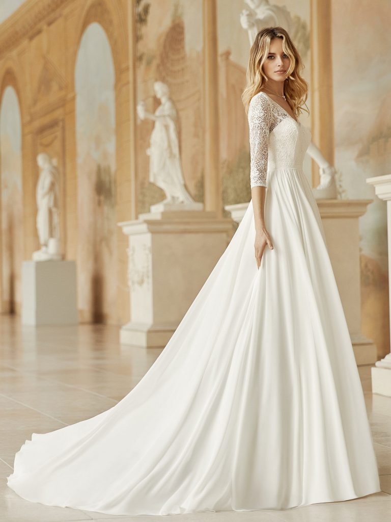 Photo shows a side view of a bride wearing Bianco Evento's "Medusa" wedding dress. The bridal gown has a lace bodice with a v-neckline and 3/4 length sleeves, and a plain chiffon skirt.