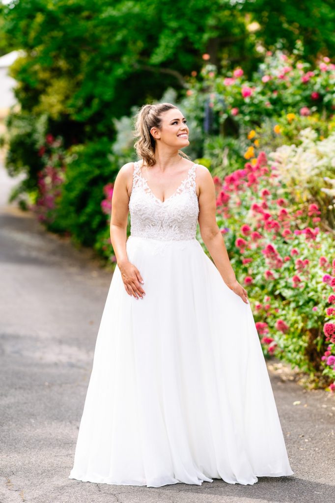 Photo shows a bride wearing an ivory A-line wedding dress with a beaded v-neck bodice and plain chiffon skirt. The dress is called Shine On by Purple Fox Bride