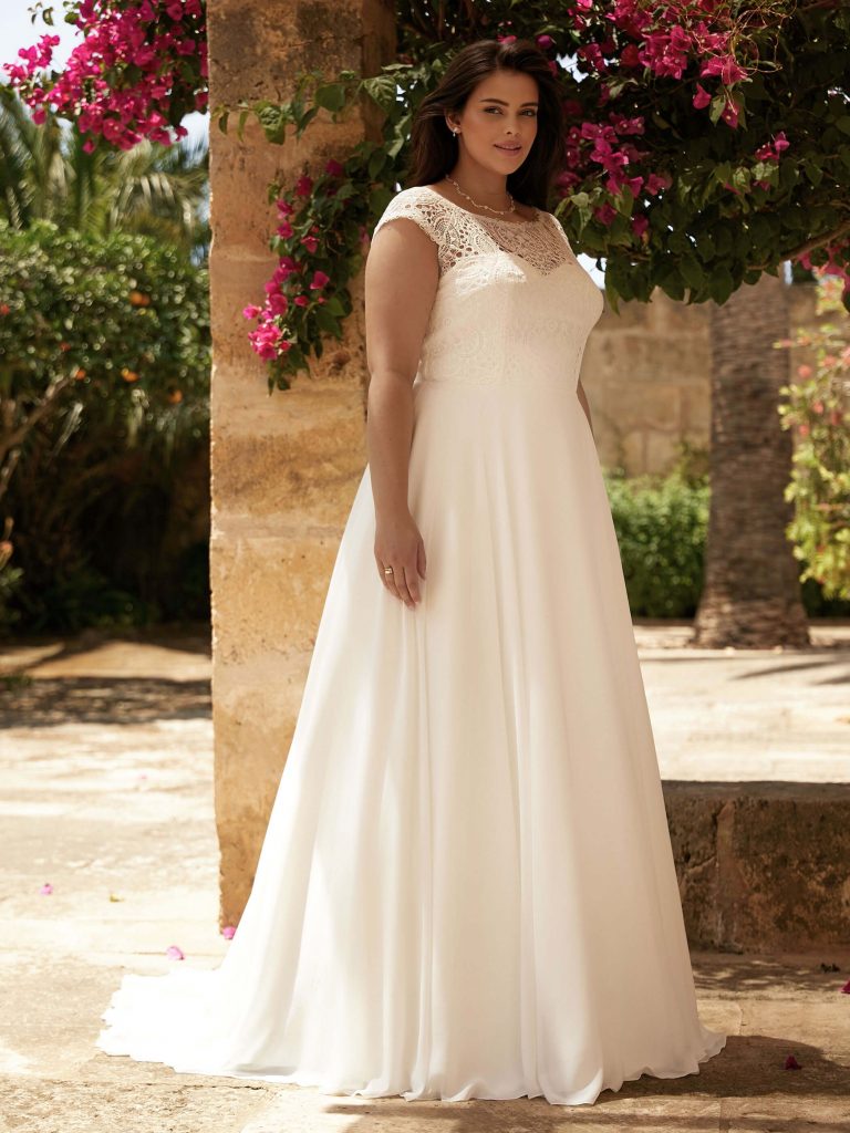 Photo of bride in a garden wearing Bianco Evento's Claudia wedding dress which features a lace bateau neckline, cap sleeves, and plain chiffon skirt.