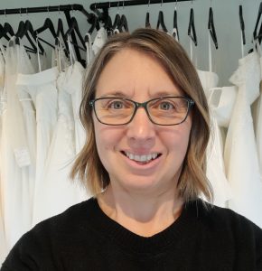 Head and shoulders photo of Vicky, owner of Lucky Sixpence Bridal. She has bobbed brown hair, green rimmed glasses, and she is wearing a black jumper.