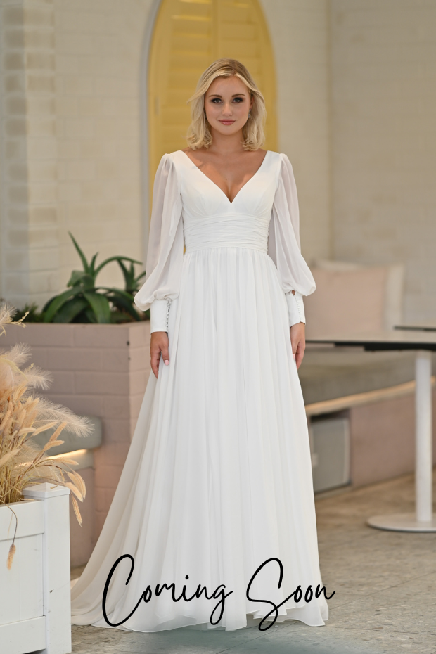 Photo shows a bride wearing an ivory chiffon wedding dress by Purple Fox. Missing Angel is a plain chiffon gown featuring a v-neckline, long sleeves with cuffs, a gathered chiffon waistline, and plain A-line skirt.