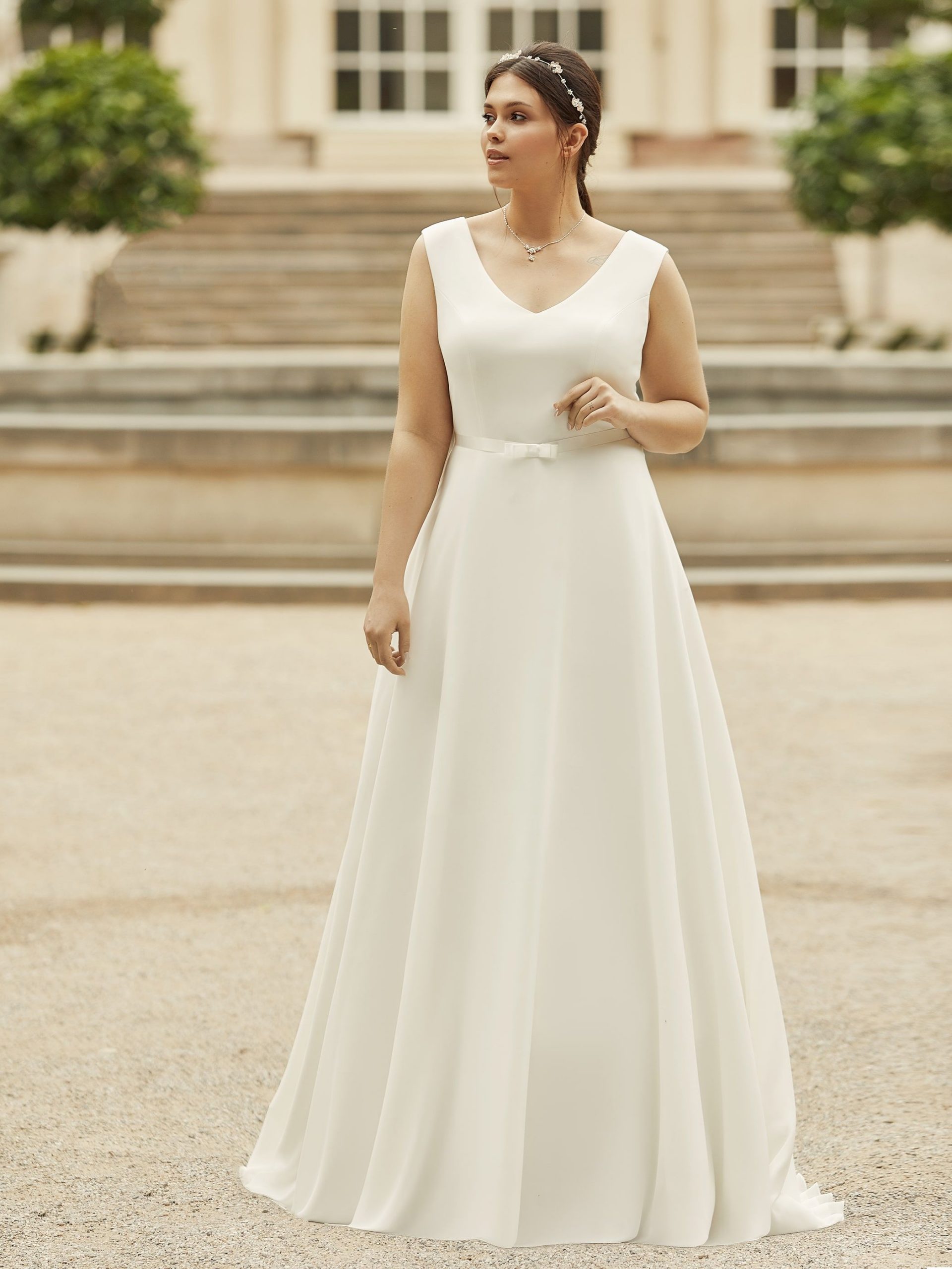 Photo shows a bride wearing a plain ivory chiffon wedding dress by Bianco Evento. Dalila features a v-neckline, wide shoulder straps, and plain A-line skirt.