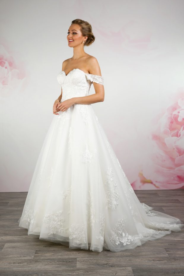 BL348 by Emma Bridals is a traditional ballgown dress with a modern off-the-shoulder neckline, and a gorgeous fitted bodice, leading to a soft tulle and boho lace skirt. Secured with a zip and buttons at the back.