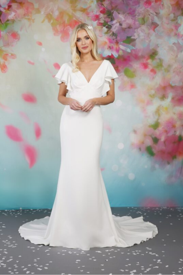 BL304 is a plain ivory fit and flare wedding dress by Emma Bridals made from the softest jersey. It features soft flutter sleeves, a v-neckline with an under-bust panel and a plain skirt. The gown is finished with plain buttons down the centre back, interspersed with diamante buttons for extra sparkle.