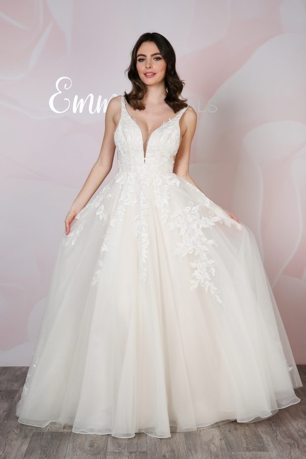Photo shows Emma Bridals BL399, a pretty A-line wedding dress featuring a soft lace bodice and lace appliques down the tulle skirt, a plunge neckline and V-back; low sides are held together with nude tulle panels for extra comfort.