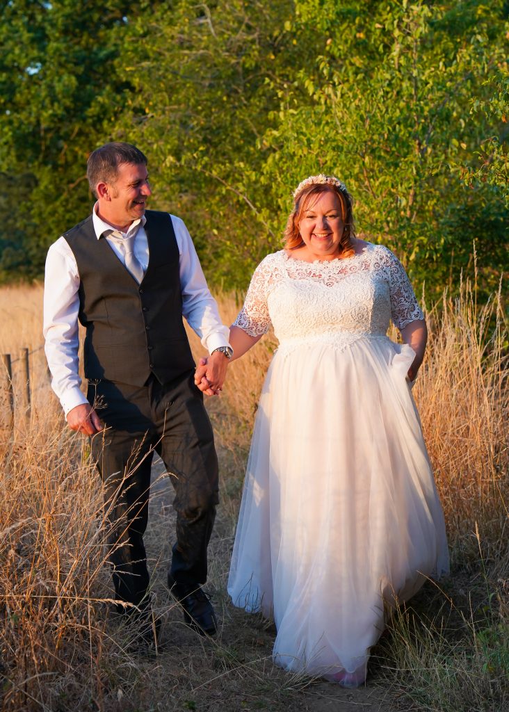 Photo of one of our real Lucky Sixpence brides holding hands with her new husband, walking in a meadow.