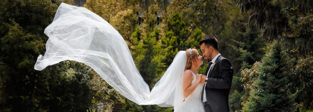 The Lucky Sixpence Bridal guide to veils. Photo shows a bride and groom holding hands and looking into each others' eyes. The brides long veil is blowing in the air behind her.