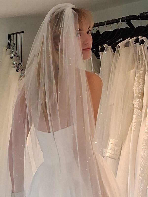 Photo shows model looking over her right shoulder at the camera wearing an ivory cut-edge veil with scatter pearls.